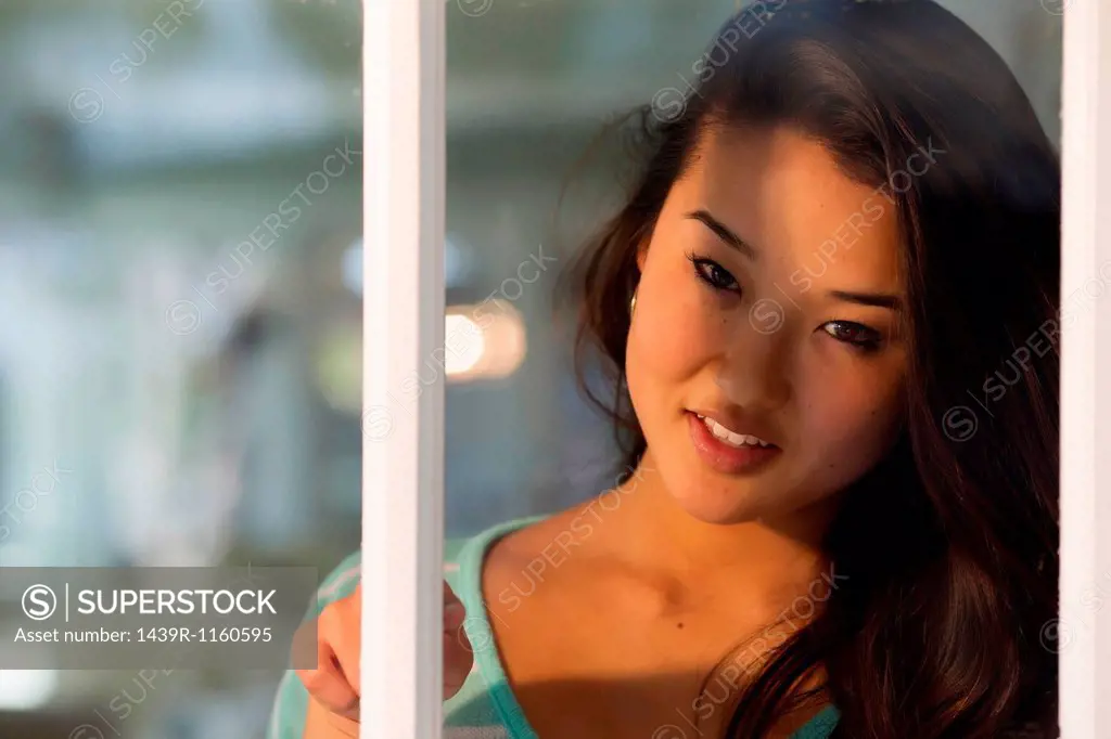 Portrait of young woman looking through window smiling