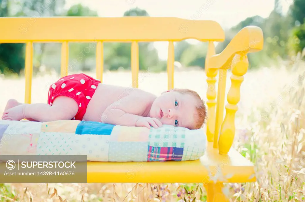 Newborn baby girl lying on yellow bench in field