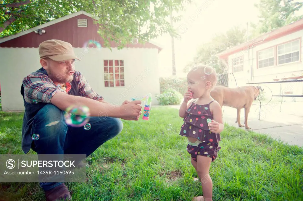 Father and baby daughter playing with bubbles in garden