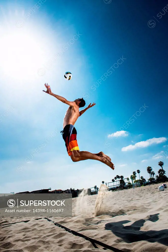 Male beach volleyball player jumping mid air to hit ball