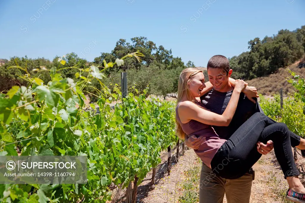 Young couple in vineyard, man carrying woman