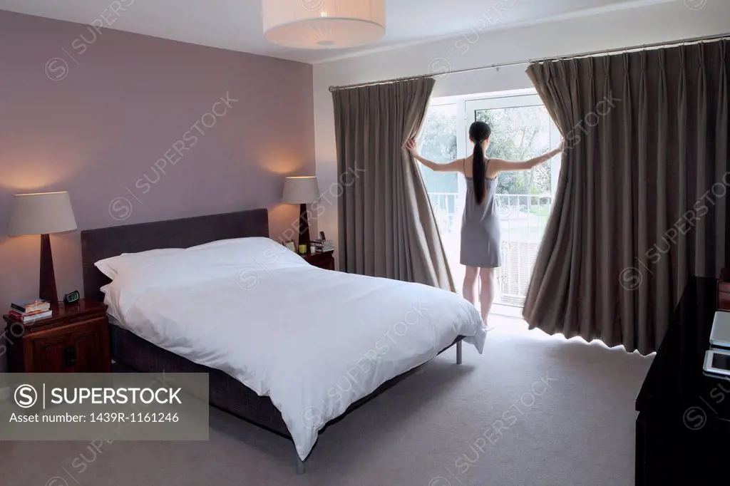 Woman drawing open curtains of bedroom