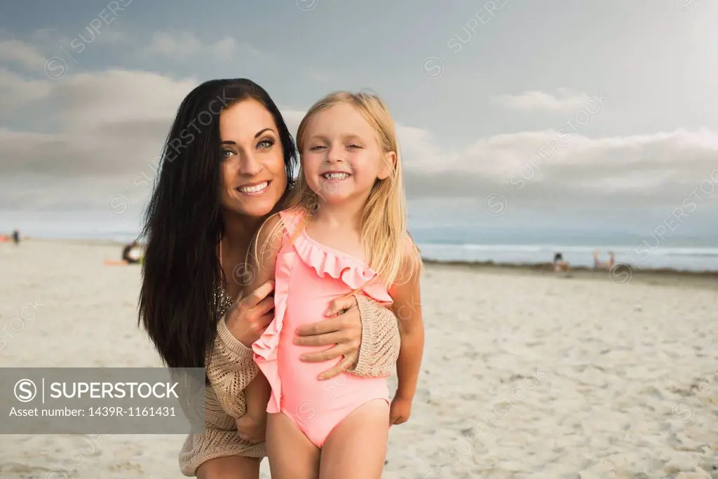 Young woman smiling with daughter on beach, portrait