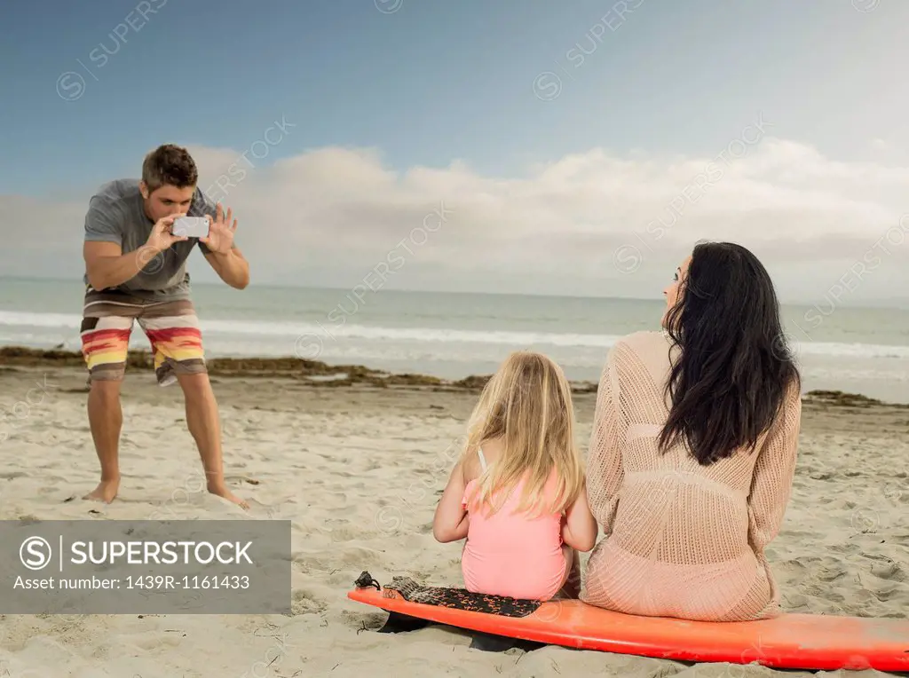 Man photographing family as the sit on a surfboard