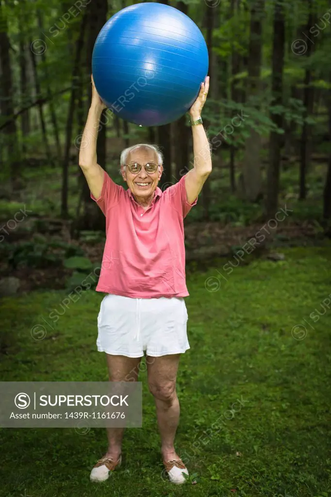 Senior man holding up exercise ball, portrait