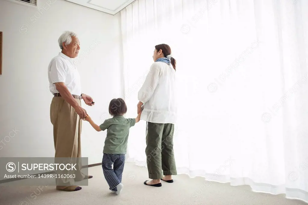 Three generation family standing by window holding hands