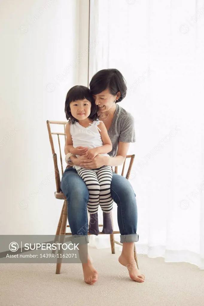 Mother and daughter sitting on wooden chair, portrait
