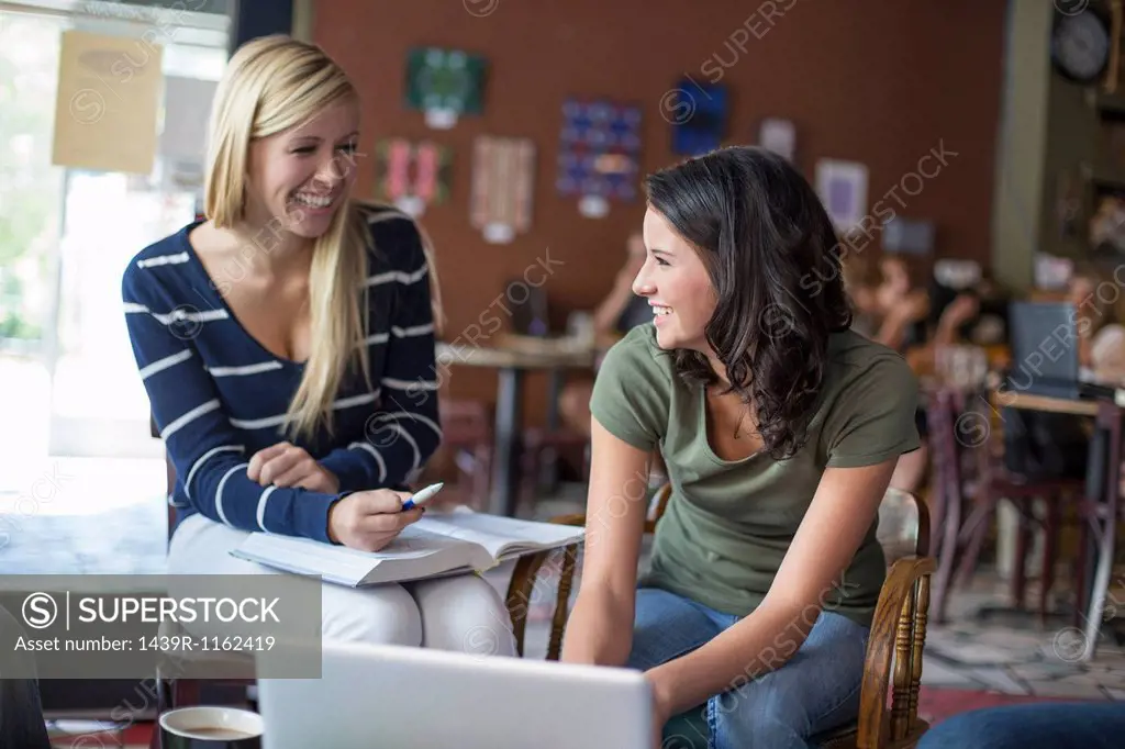 Two teenagers studying with textbooks and computer in cafe