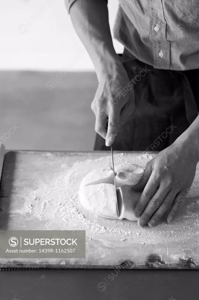 Mid adult baker slicing fresh dough