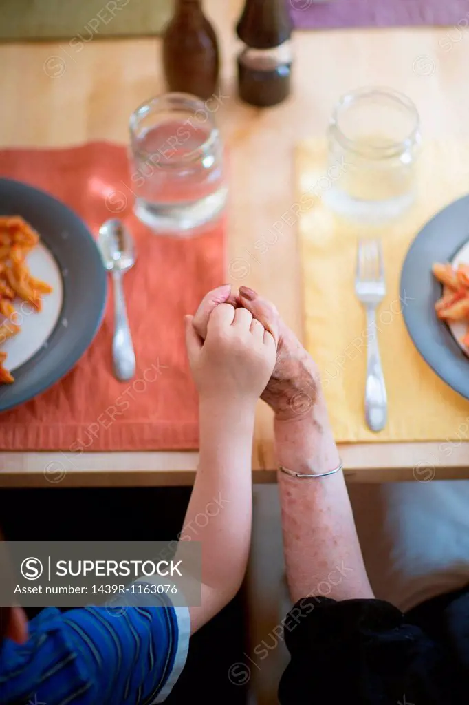 Grandmother and grandson holding hands at dinner table