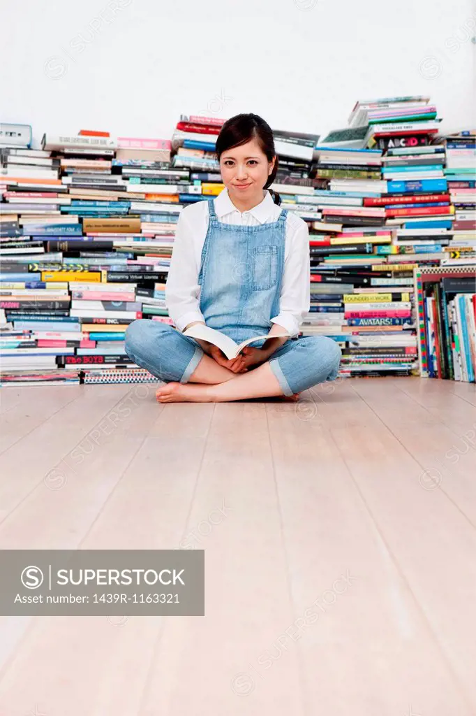 Young woman crossed legged on floor in front of book pile