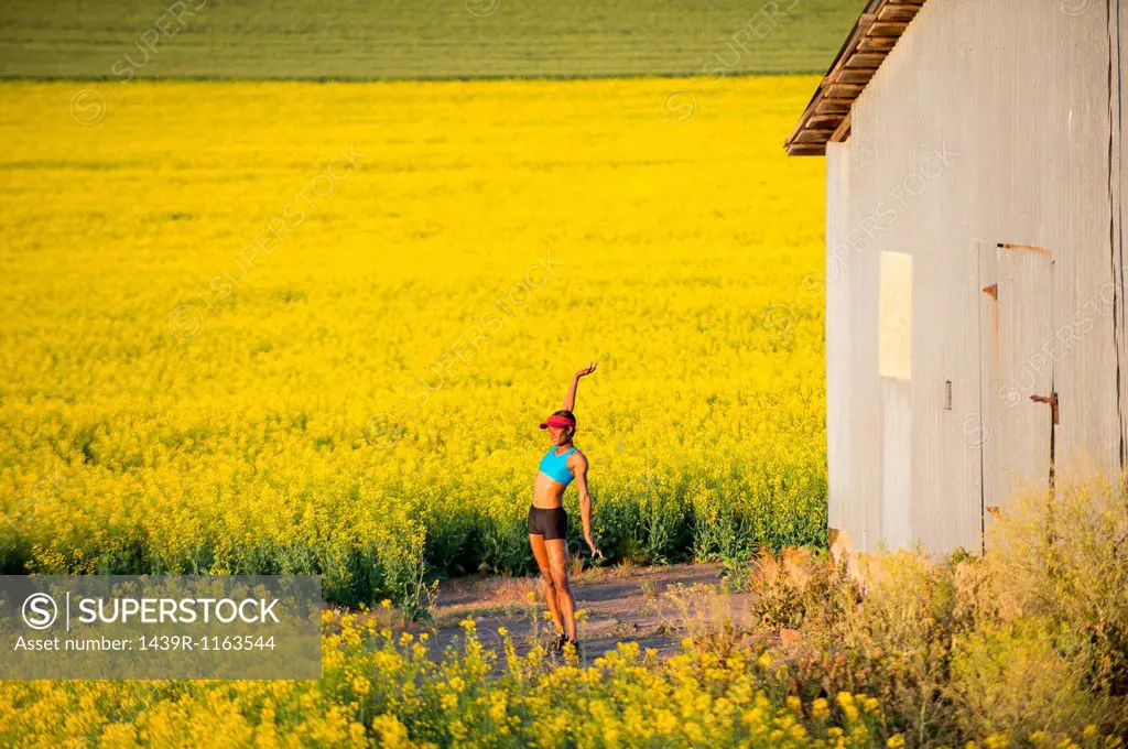 Young woman runner stretching in field of oil seed rape