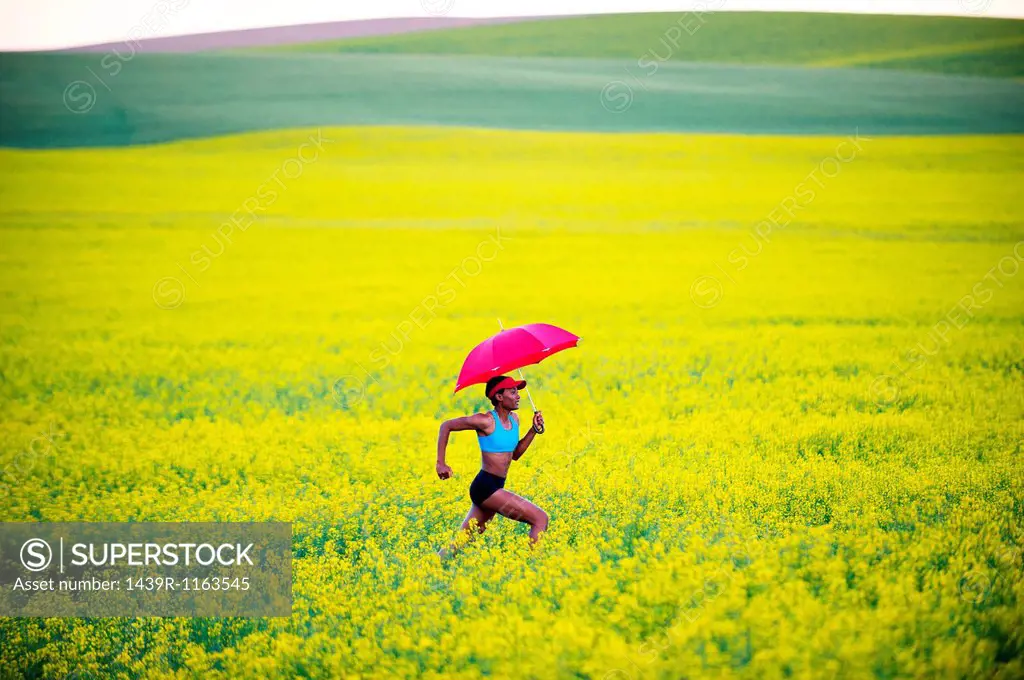 Young woman running in oil seed rape field with red umbrella