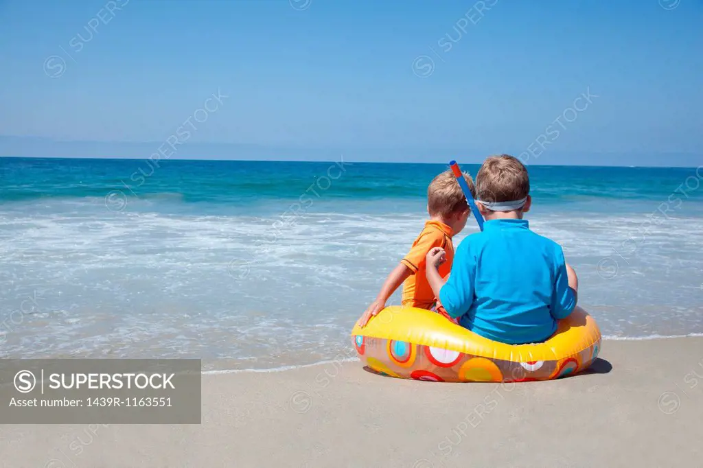 Two young brothers sitting on rubber ring at beach
