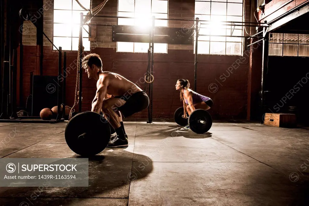 Two young adults working out with barbells in gym