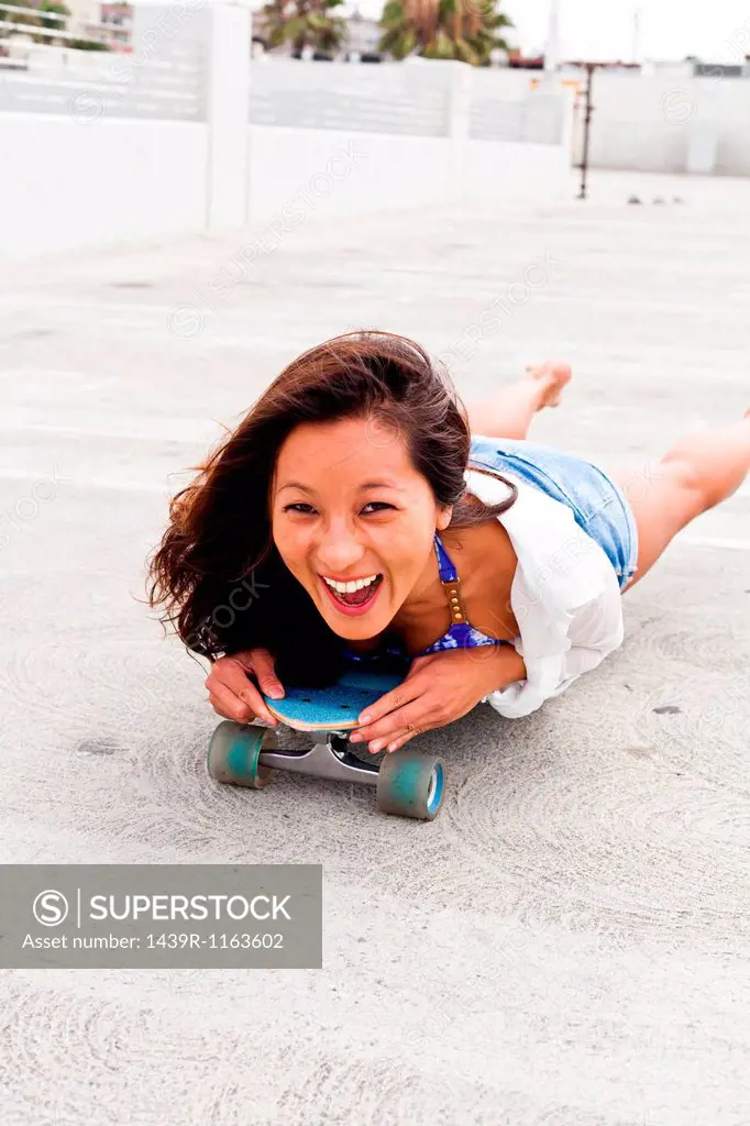 Woman in parking lot lying on skateboard