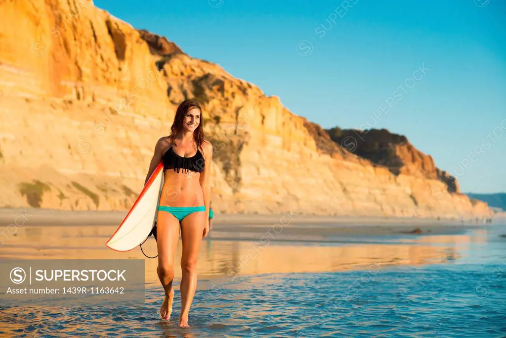 Young woman walking with surfboard, La Jolla, San Diego, California, USA