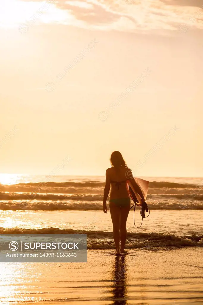 Young woman with surfboard at sunset, La Jolla, San Diego, California, USA