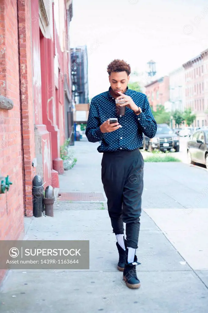 Young man walking down street with cellphone and drink