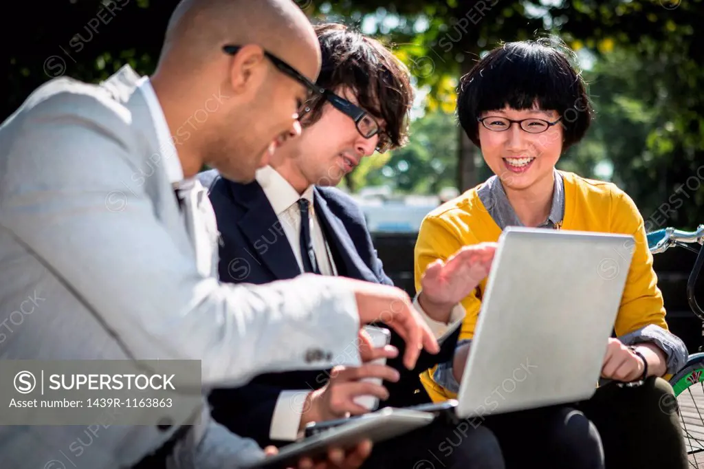 Three casual businesspeople using laptop in park