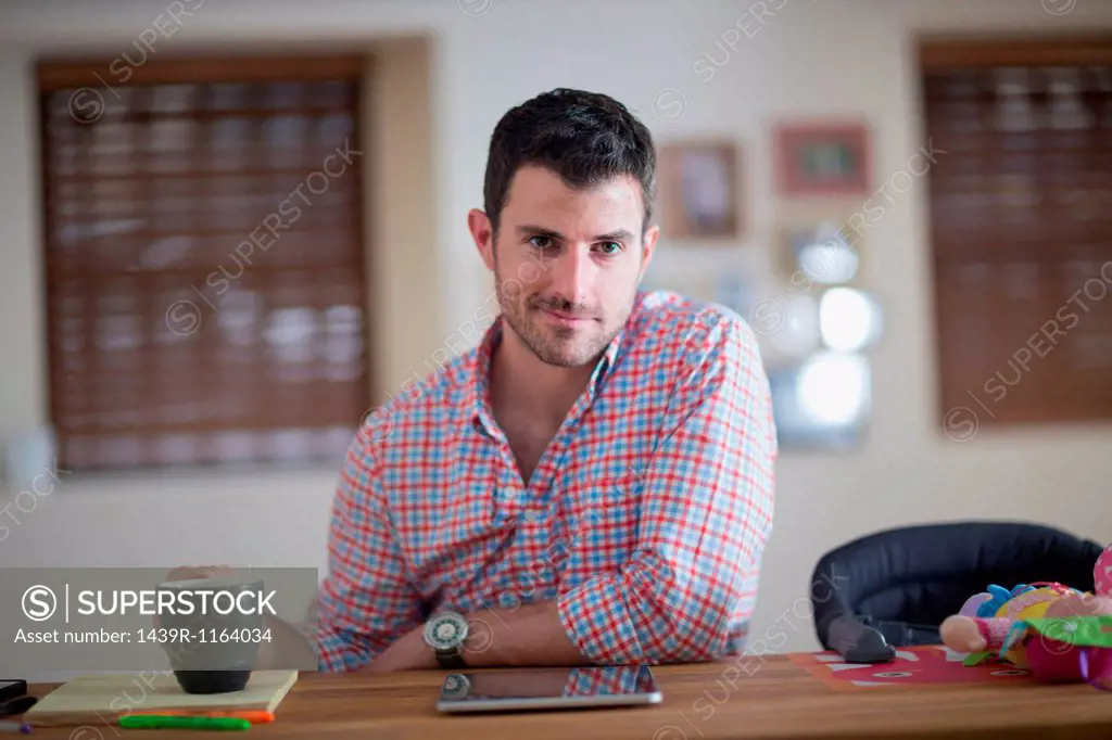Man sitting at kitchen counter with cup of coffee and digital tablet