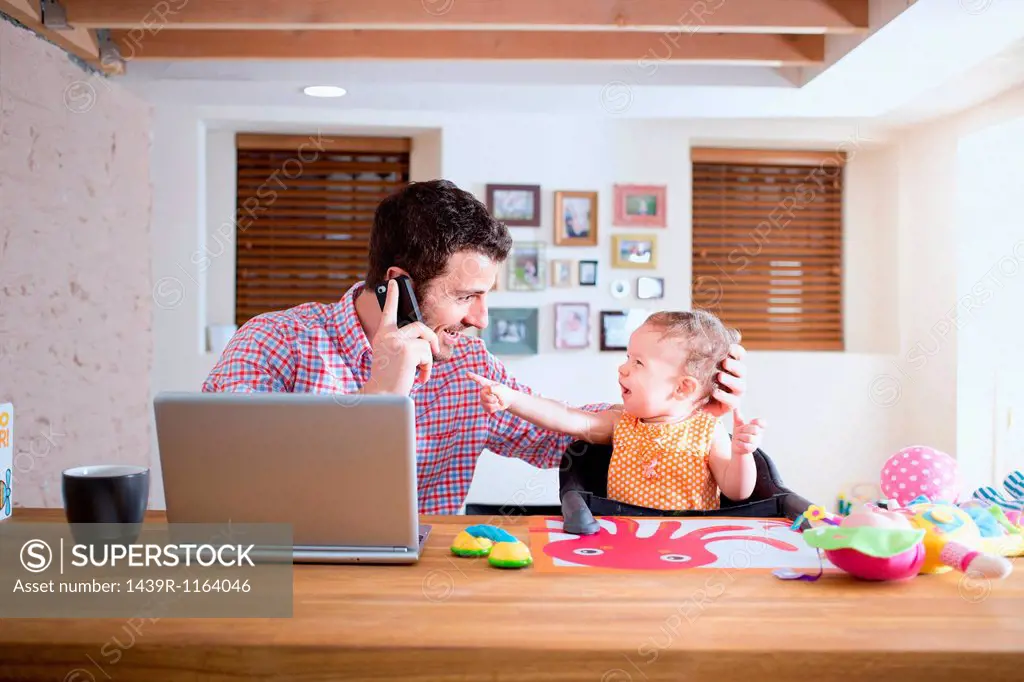 Man and baby sitting at kitchen counter making phone call