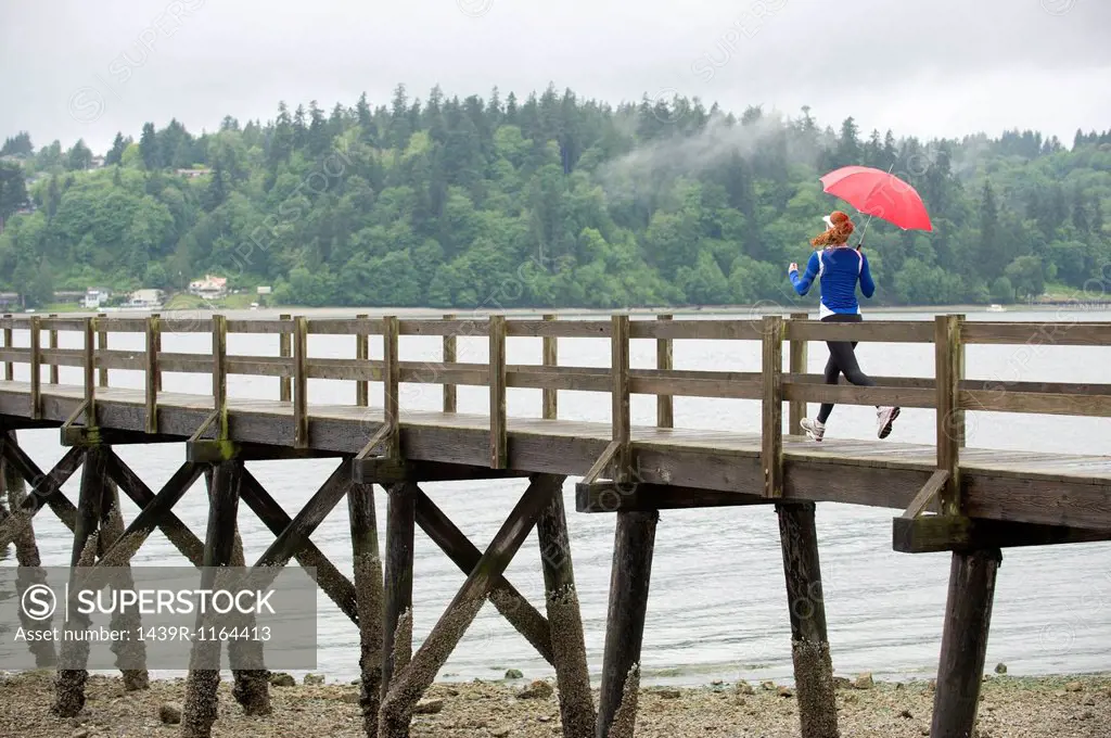 Teenage girl running with umbrella on pier, Bainbridge Island, Washington, USA