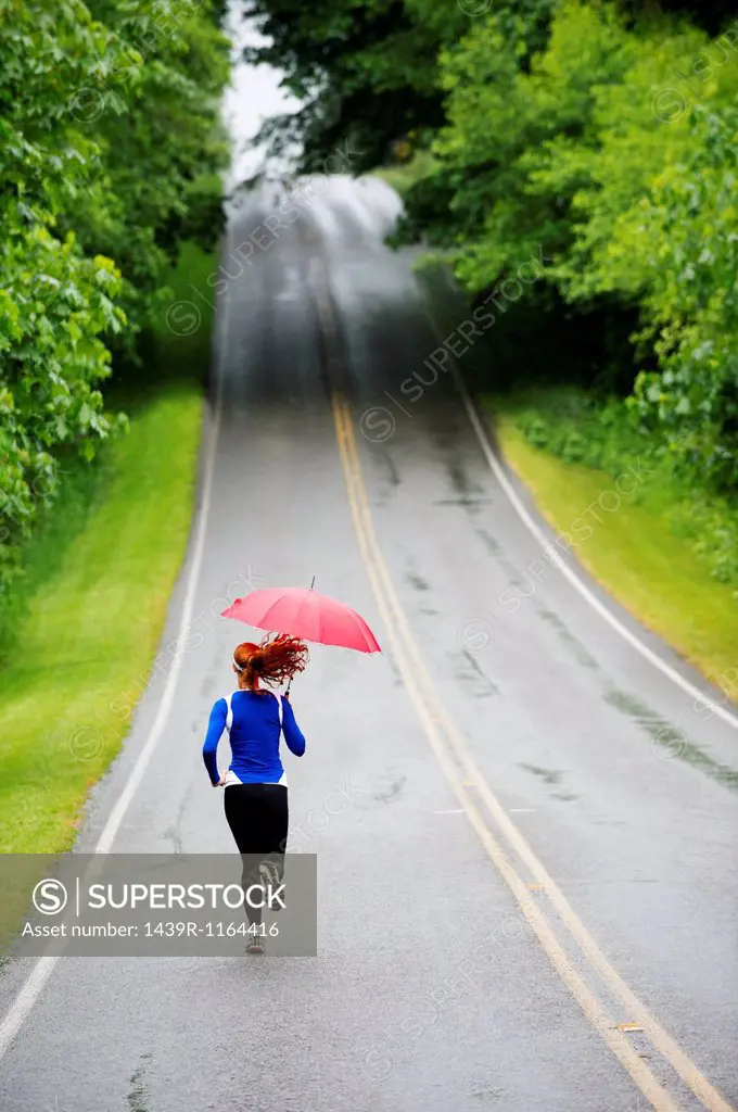 Teenage girl running with umbrella on road, Bainbridge Island, Washington, USA