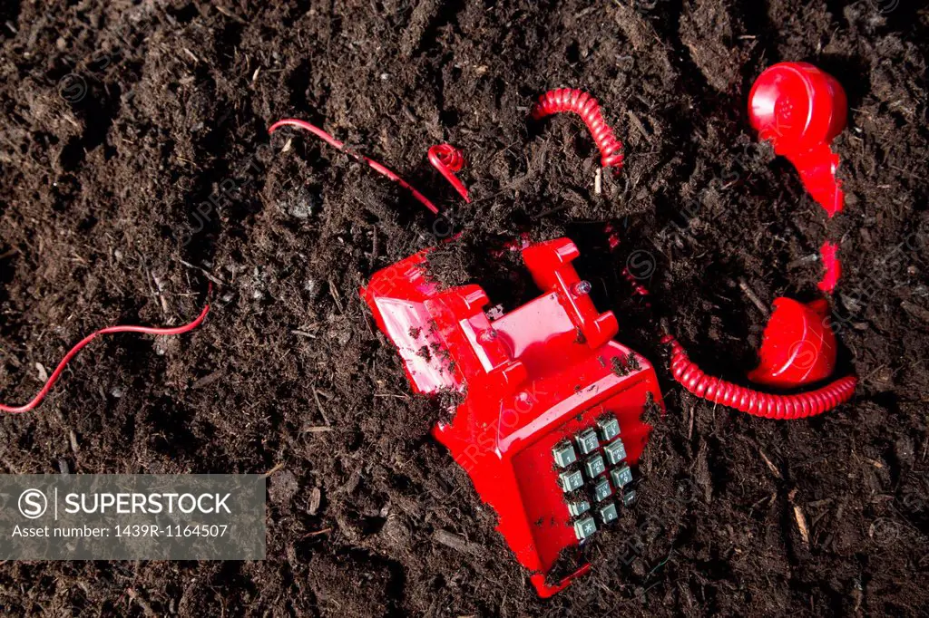 Red retro telephone buried in soil