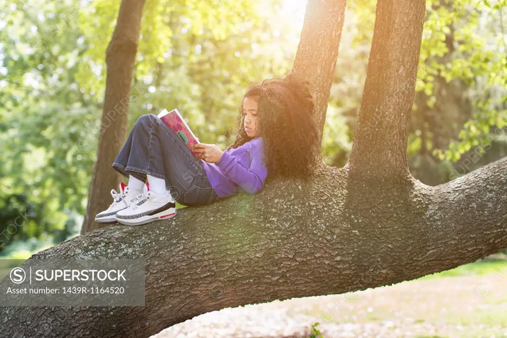Young girl lying on tree branch reading book