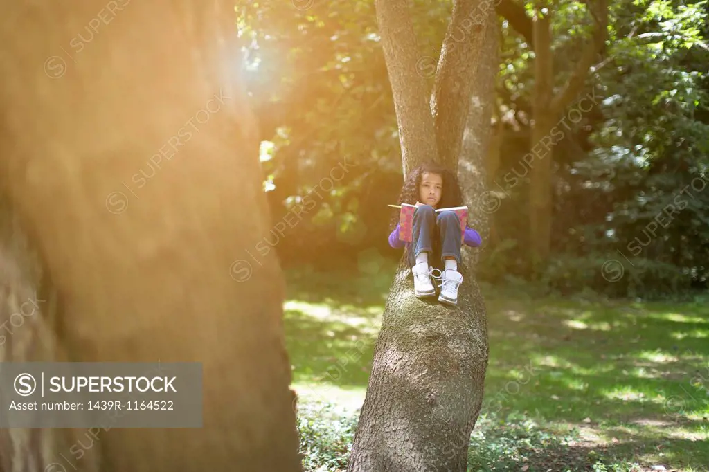 Young girl lying on tree branch looking at book