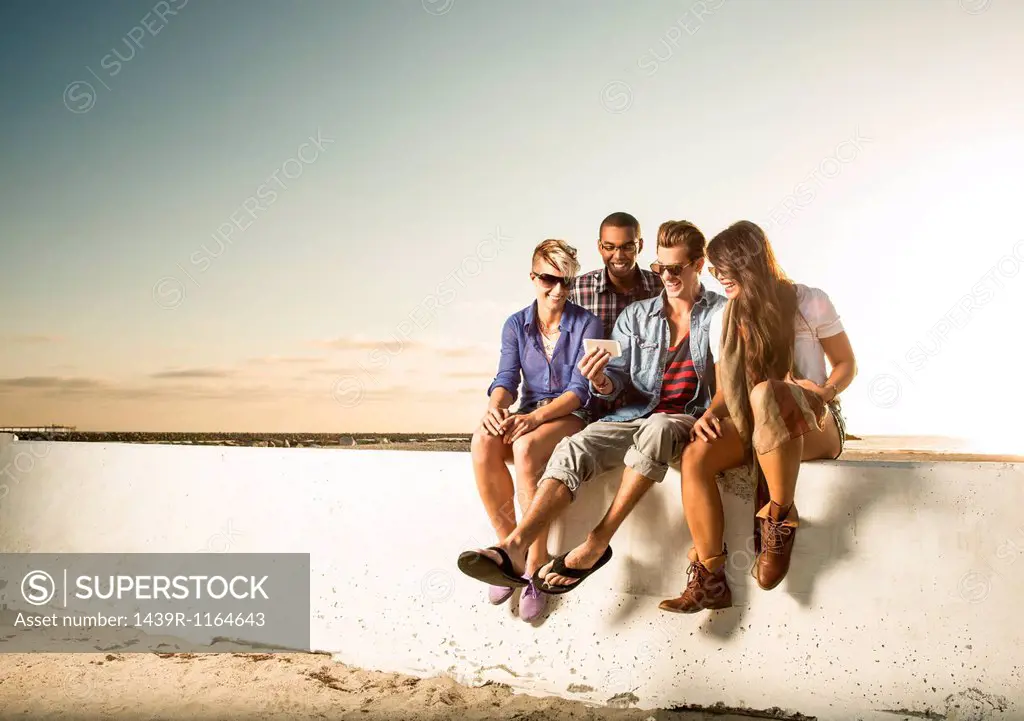 Friends sitting on wall with smartphone, Mission Beach, San Diego, California, USA