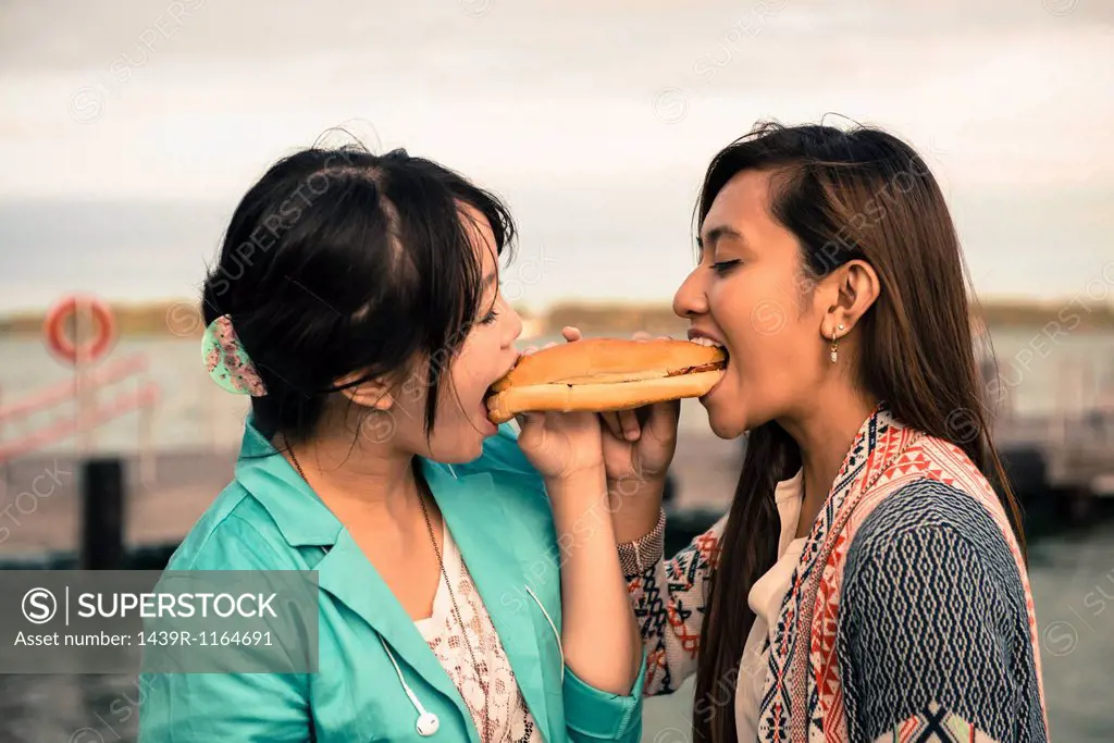 Young women biting opposite ends of sandwich