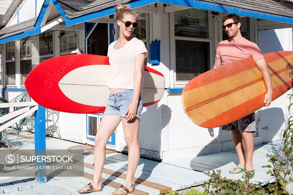 Couple on patio carrying surfboards, Breezy Point, Queens, New York, USA