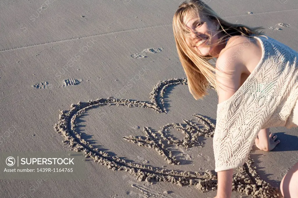 Smiling woman writing love message in sand, Breezy Point, Queens, New York, USA