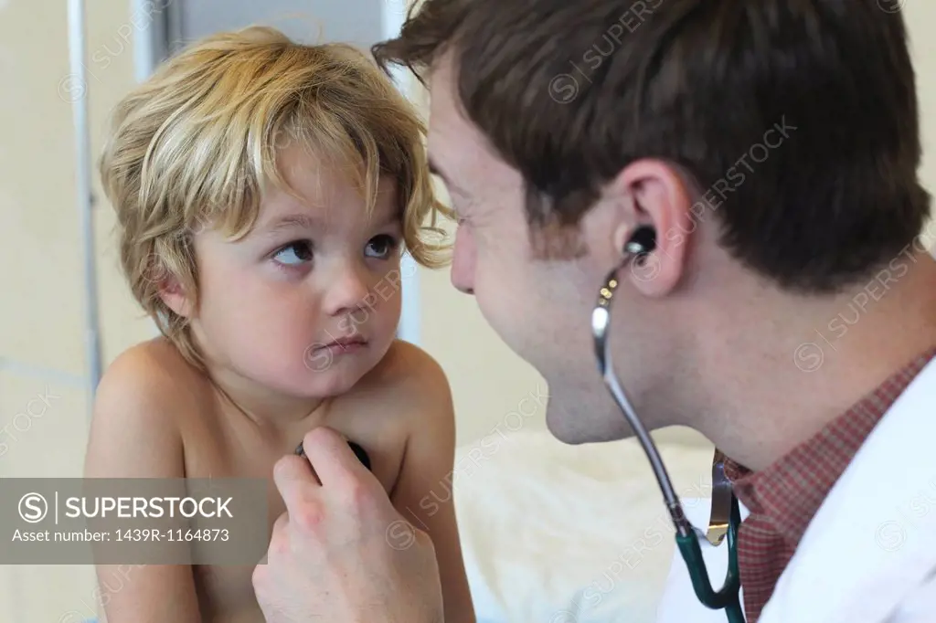 Young male doctor listening to boys chest in clinic
