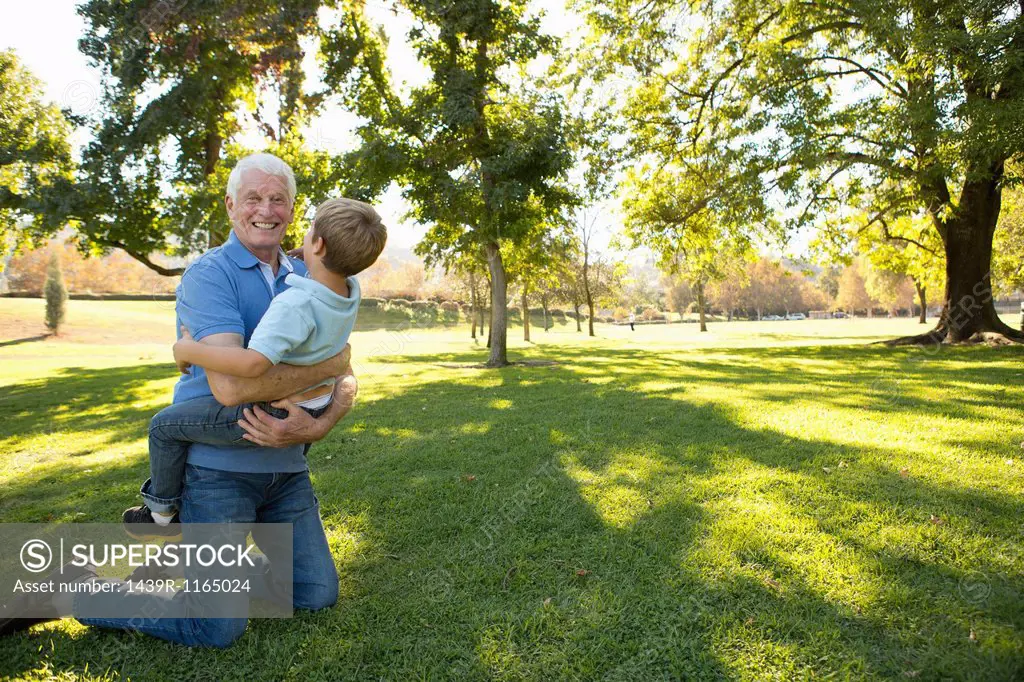 Grandfather kneeling on grass hugging grandson