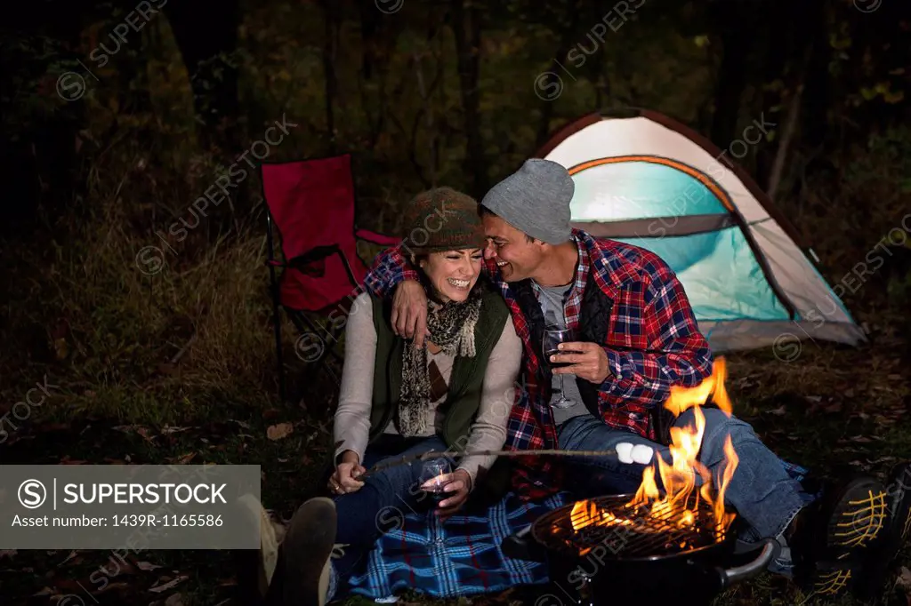 Mature couple sitting outside tent with barbecue and glass of wine
