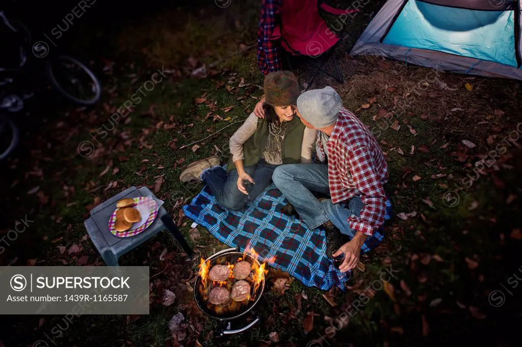Mature couple sitting outside tent with barbecue and glass of wine