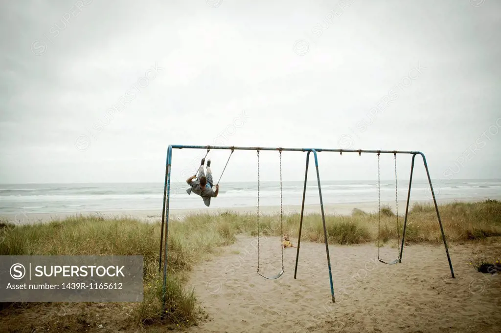 Female toddler watching father on beach swing