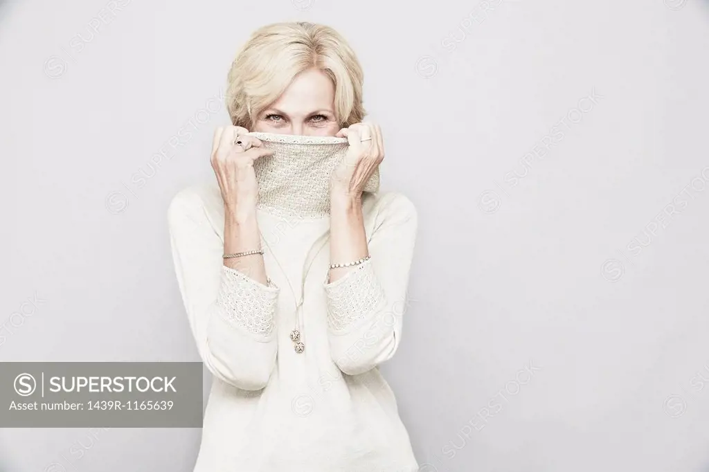 Studio portrait of senior woman hiding behind roll neck