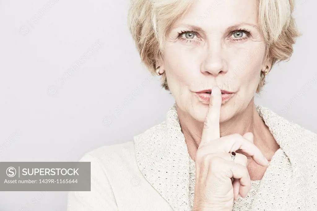 Cropped studio portrait of senior woman with finger on lips