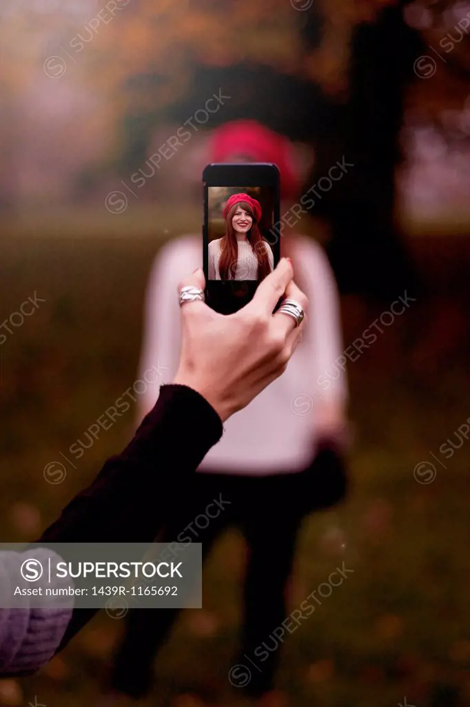 Hand holding smartphone, taking photograph of young woman