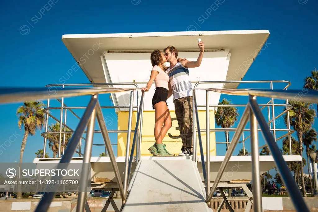 Young couple kissing at San Diego beach, taking self portrait photograph
