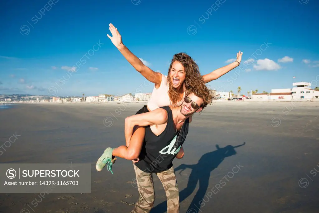 Young woman on boyfriend´s back with arms raised