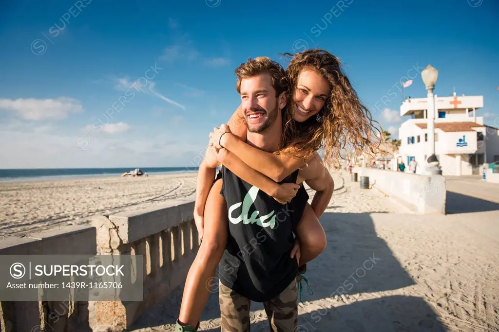 Young man giving girlfriend a piggy back at San Diego beach