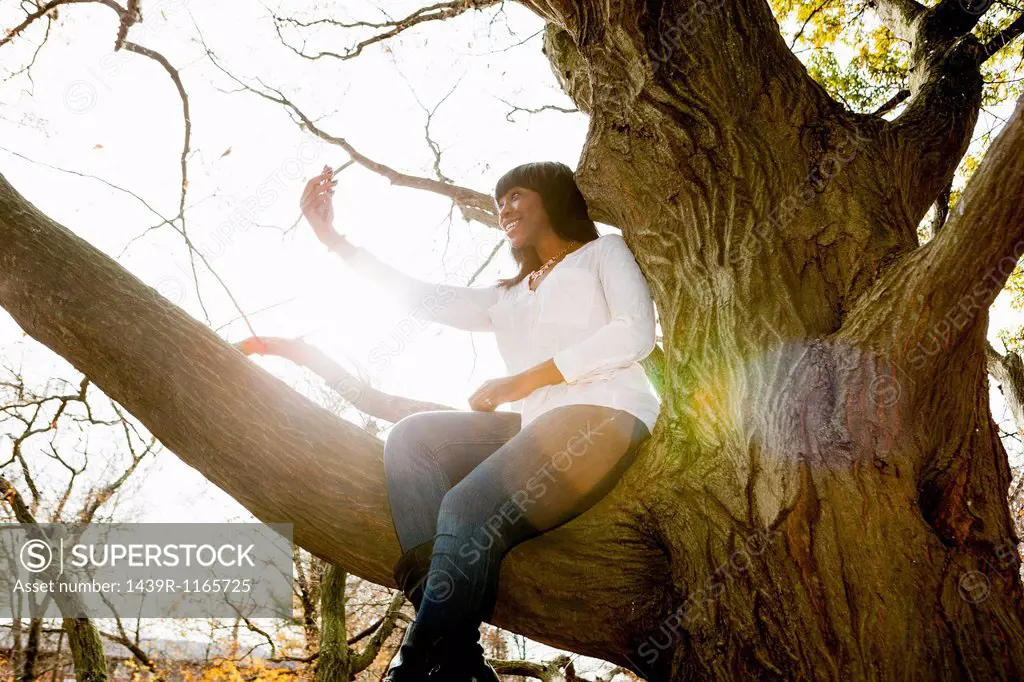 Young woman taking self portrait whilst sitting in park tree
