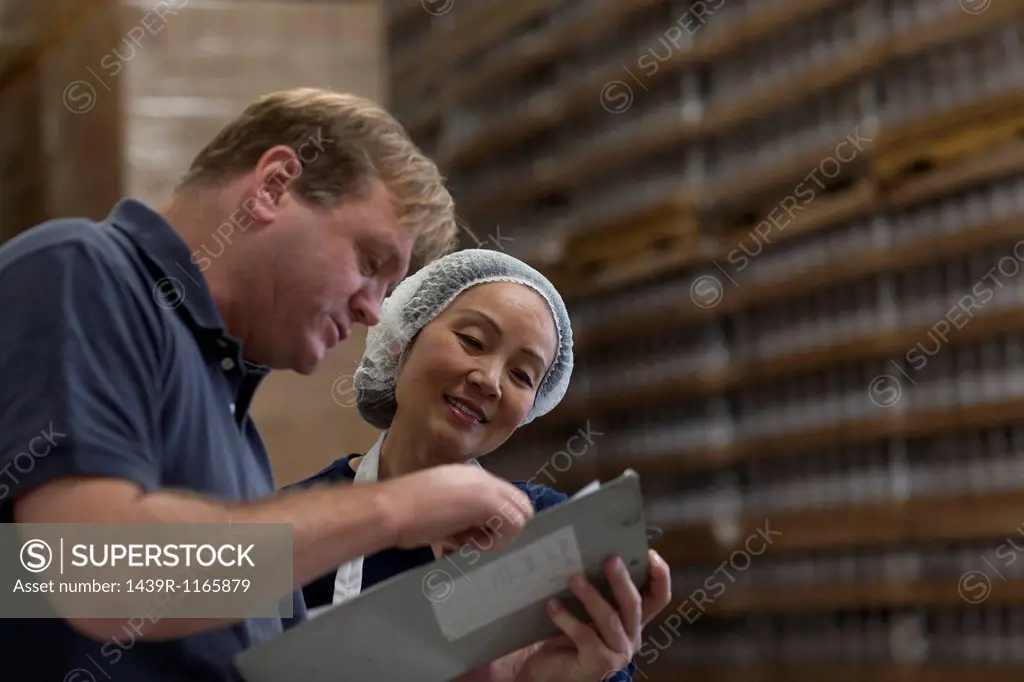 Factory worker and manager looking at clipboard in warehouse
