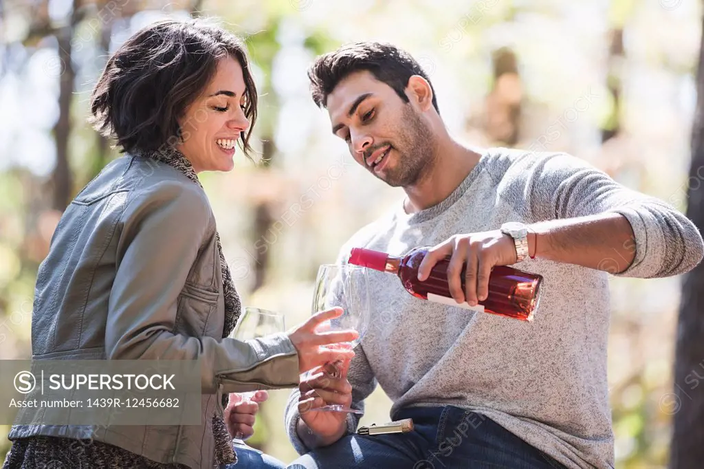 Couple pouring bottle of rose wine in forest
