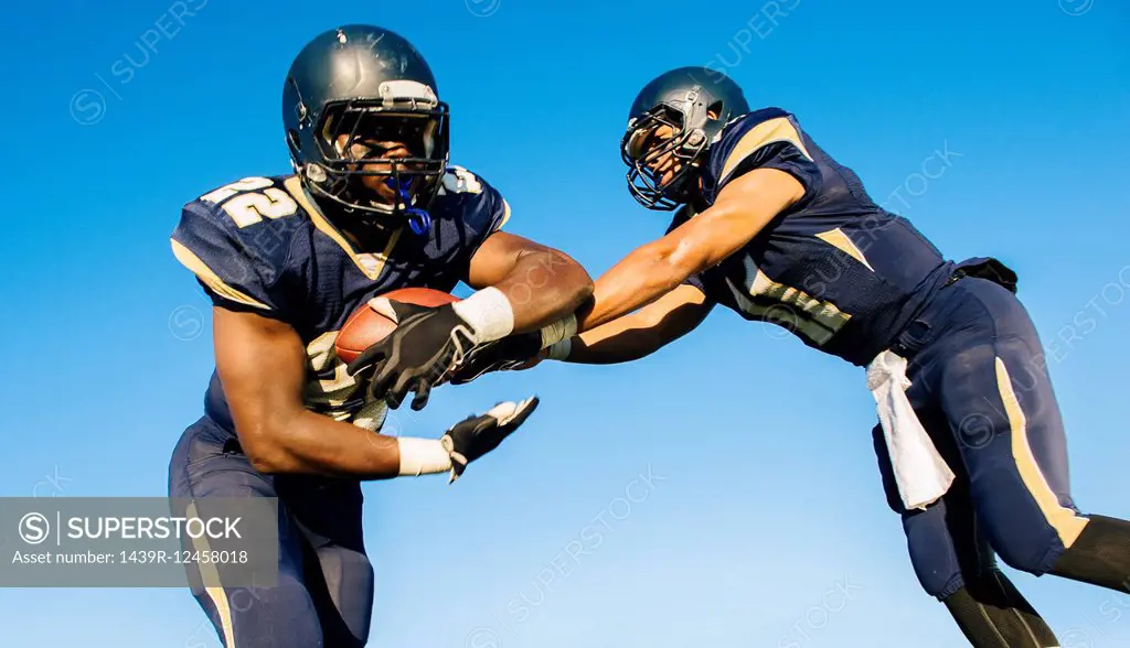 Two teenage american football players tackling ball